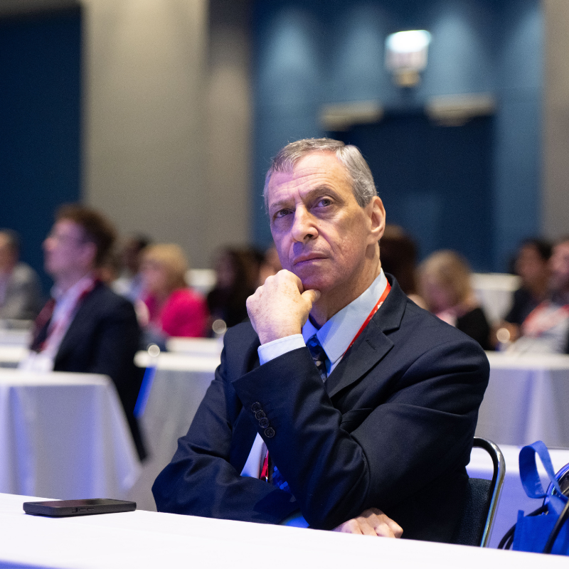 An attendee listens attentively during a Heart Rhythm 2026 session, with other conference participants visible in the background.